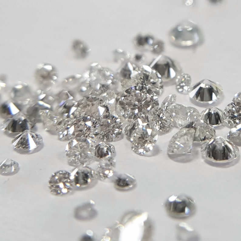 May include: A collection of loose, clear, faceted diamonds of various sizes, scattered on a white surface.