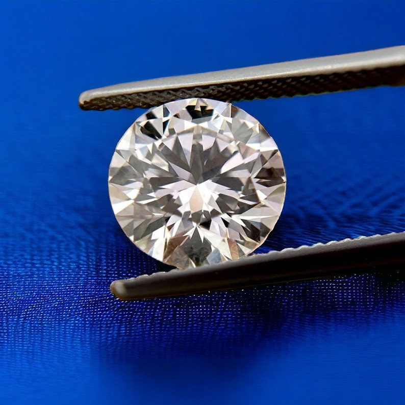 May include: A large, clear, round diamond held by silver tweezers against a blue background.