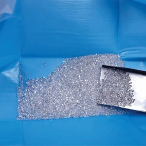 May include: A blue tray filled with a large quantity of small, clear, faceted crystals. A metal scoop is partially submerged in the crystals.