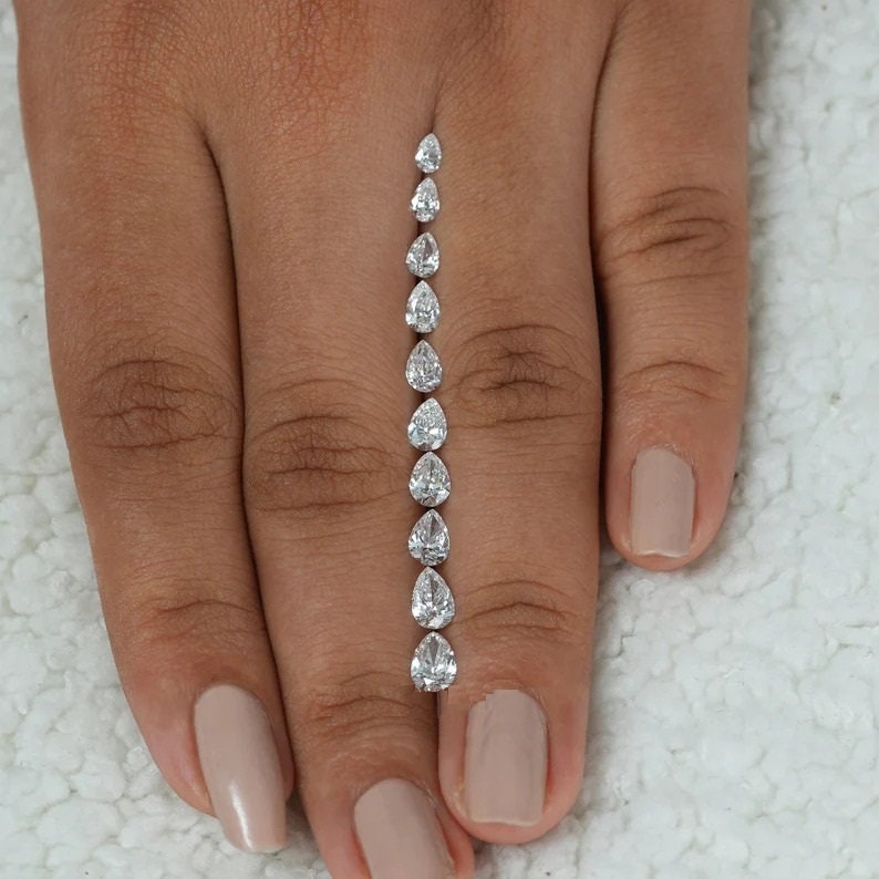 May include: A line of pear-shaped diamonds of varying sizes, arranged in a vertical line on a person's finger.