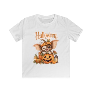 Puede incluir: Una camiseta blanca de manga corta con el gráfico de una criatura guiñando un ojo con orejas grandes sentada dentro de una calabaza tallada. El diseño incluye hojas de otoño, una pequeña linterna y el texto naranja Halloween sobre la criatura.