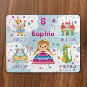 May include: A blue and white personalized puzzle featuring a princess, a castle, a dragon, a carriage, and a giraffe. The puzzle says "S is for Sophia" and includes the phrases "Sophia is cute", "Sophia is kind", "Sophia is smart", and "Sophia is brave".