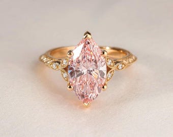 May include: A marquise-cut pink gemstone ring with a gold band. The ring features a detailed filigree design with small accent stones. The gemstone is a light pink color and is the focal point of the ring.