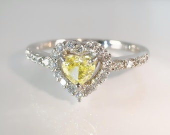 May include: A heart-shaped yellow diamond ring with a halo of smaller diamonds. The ring's band is also adorned with small diamonds. The ring is set in a silver metal.