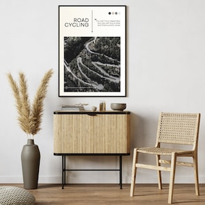 Puede incluir: Una fotograf&iacute;a en blanco y negro de un camino sinuoso en las monta&ntilde;as. La foto est&aacute; enmarcada y colgada en una pared sobre un armario de madera. El texto "ROAD CYCLING" y una cita sobre la felicidad est&aacute;n impresos en el marco.