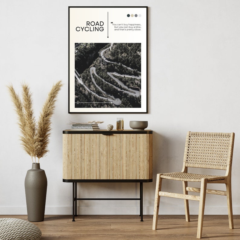Puede incluir: Una fotograf&iacute;a en blanco y negro de un camino sinuoso en las monta&ntilde;as. La foto est&aacute; enmarcada y colgada en una pared sobre un armario de madera. El texto "ROAD CYCLING" y una cita sobre la felicidad est&aacute;n impresos en el marco.