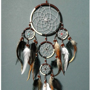 A brown black cream dreamcatcher with 5 rings, the main top ring is 12cm wide. All rings have silver webs with a central bead. Four rings hang below the top ring, all decorated with beads natural white, black and brown feathers. Total length 35cm