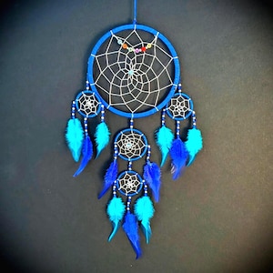 May include: A blue dreamcatcher with a circular frame and a white web design. It features multiple smaller dreamcatchers and blue and turquoise feathers. The dreamcatcher is suspended against a dark background.
