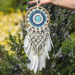 May include: A white dream catcher with blue and white crocheted details and white feathers hanging from it.