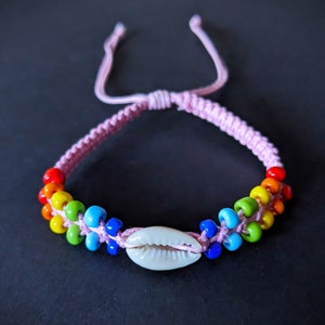 May include: A pink braided bracelet with rainbow coloured beads and a white seashell charm.