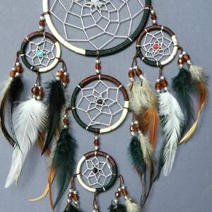 May include: A handcrafted dreamcatcher with a central web design and multiple smaller hoops. The dreamcatcher features a combination of white, brown, and black accents, adorned with feathers and beads. The design incorporates a variety of colors and textures.