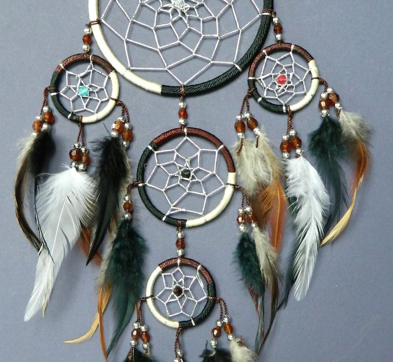 May include: A handcrafted dreamcatcher with a central web design and multiple smaller hoops. The dreamcatcher features a combination of white, brown, and black accents, adorned with feathers and beads. The design incorporates a variety of colors and textures.