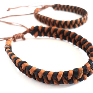 May include: Two braided leather bracelets in black and brown. The bracelets are made of thin leather cords woven together in a simple pattern.