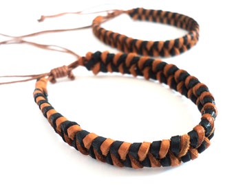 May include: Two braided leather bracelets in black and brown. The bracelets are made of thin leather cords woven together in a simple pattern.