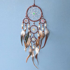 Brown dreamcatcher with 5 rings. The top ring is 9cm wide. All rings have silver webs with a central bead. Four rings hang below the top ring, strung with beads, cowrie shells and black feathers. Length 30cm