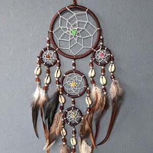 May include: A brown dream catcher with multiple hoops, white netting, and colorful beads. The dream catcher is adorned with feathers and seashells.