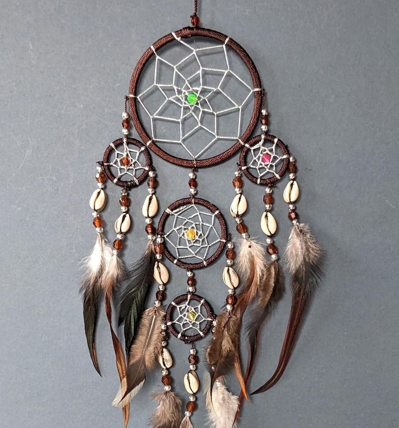 May include: A brown dream catcher with multiple hoops, white netting, and colorful beads. The dream catcher is adorned with feathers and seashells.