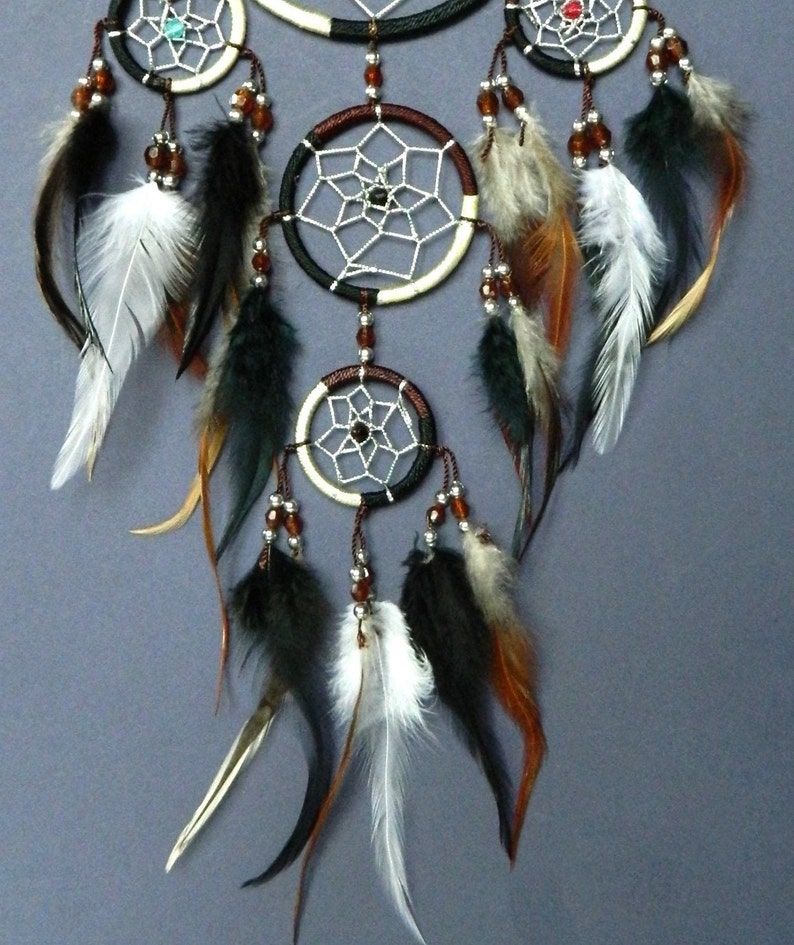 May include: A handcrafted dreamcatcher with multiple circular frames, each featuring a web-like design. The dreamcatcher is adorned with brown, black, and white feathers, along with small beads. The color palette includes shades of brown, black, white, and cream.