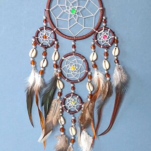 May include: A brown dream catcher with white netting, brown beads, and white feathers. The dream catcher has three smaller circles with white netting and brown beads.