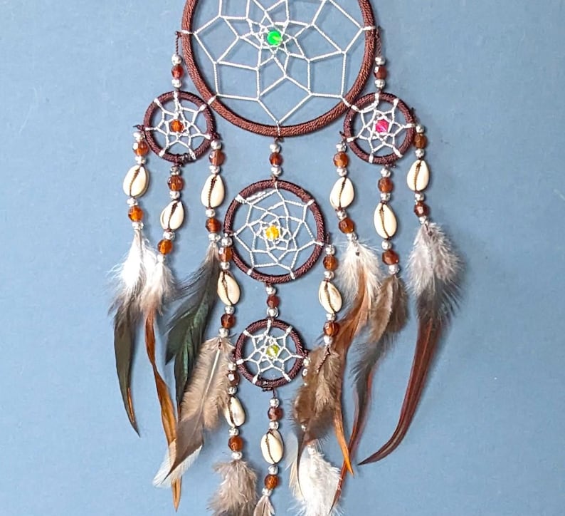 May include: A brown dream catcher with white netting, brown beads, and white feathers. The dream catcher has three smaller circles with white netting and brown beads.