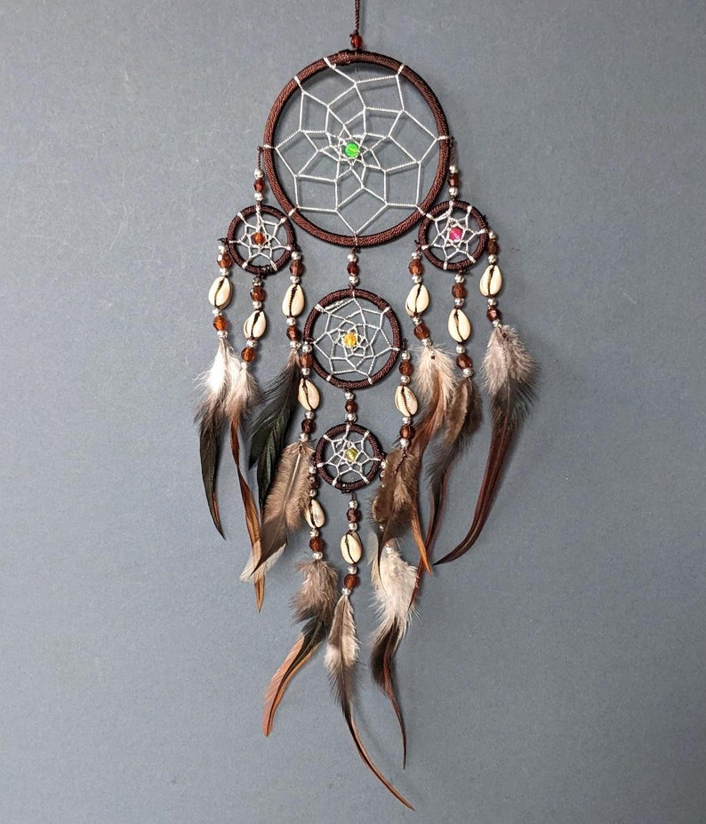 May include: A brown dream catcher with white netting and colorful beads. It has four hoops with feathers and shells hanging from the bottom.