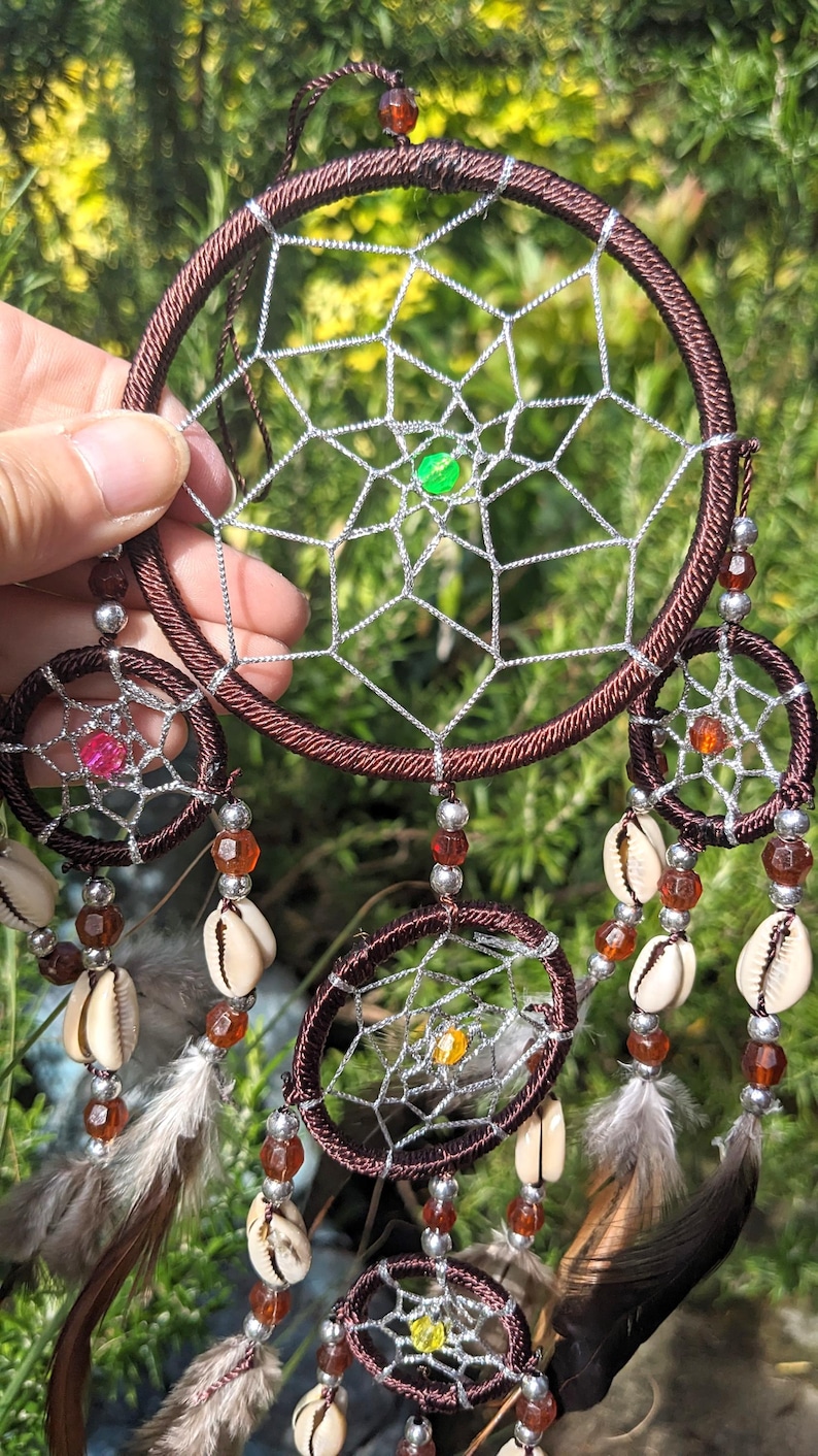 May include: A brown dream catcher with multiple layers of netting and beads. The dream catcher has a variety of shells and feathers hanging from it.