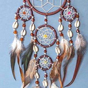 May include: A brown dream catcher with white netting and brown feathers. The dream catcher has multiple rings with beads and shells hanging from them.