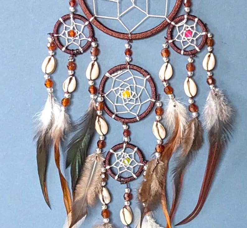 May include: A brown dream catcher with white netting and brown feathers. The dream catcher has multiple rings with beads and shells hanging from them.
