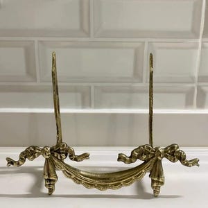 Peut inclure: Un support de photo en m&eacute;tal dor&eacute; avec un design d&eacute;coratif de n&oelig;ud et de ruban. Le support est en laiton et a un aspect vintage.