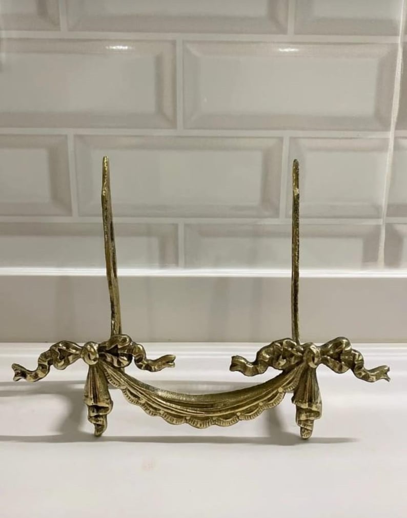 Peut inclure: Un support de photo en m&eacute;tal dor&eacute; avec un design d&eacute;coratif de n&oelig;ud et de ruban. Le support est en laiton et a un aspect vintage.
