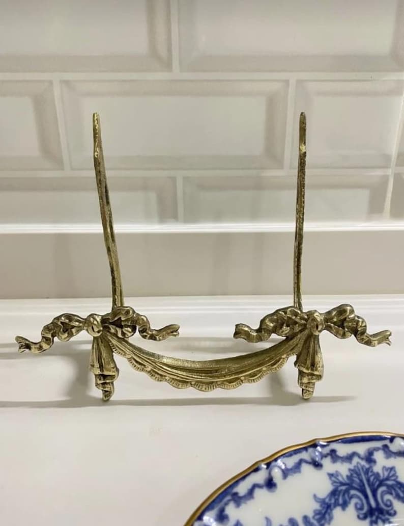 Peut inclure: Un support d&eacute;coratif en m&eacute;tal dor&eacute; avec un bord festonn&eacute; et des d&eacute;tails en ruban. Le support est con&ccedil;u pour tenir une assiette ou un autre objet d&eacute;coratif.