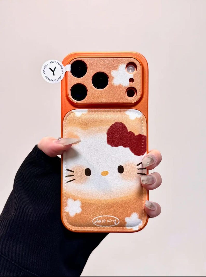 May include: Orange phone case with a Hello Kitty design. The case has a textured orange border and a white and orange background with a Hello Kitty face and a red bow. The text "Hello Kitty" is at the bottom.