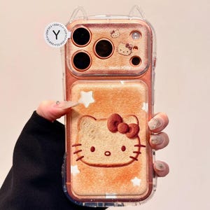 May include: A clear phone case featuring a Hello Kitty design. The case has a brown background with a Hello Kitty face and stars. The top of the case has a Hello Kitty design and the words "Hello Kitty".