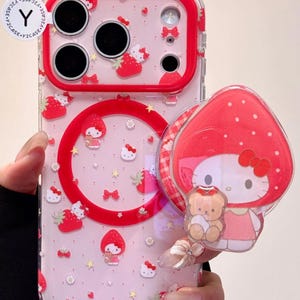 May include: Clear phone case with a red border and a strawberry and Hello Kitty design. The case has a red circle around the camera lenses and a matching pop-up grip featuring Hello Kitty and a teddy bear.