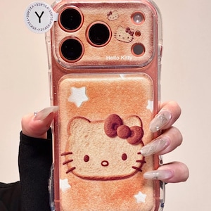 May include: Clear phone case with a Hello Kitty design. The case features a pinkish-orange background with a Hello Kitty illustration resembling a slice of bread. The case has a clear border and cat ear accents at the top. The text "Hello Kitty" is visible.