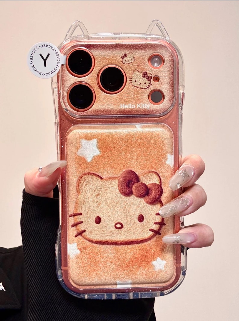 May include: Clear phone case with a Hello Kitty design. The case features a pinkish-orange background with a Hello Kitty illustration resembling a slice of bread. The case has a clear border and cat ear accents at the top. The text "Hello Kitty" is visible.