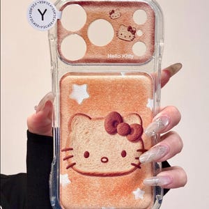 May include: Clear phone case with a Hello Kitty design. The case features a light brown background with a Hello Kitty face and stars. The top section has a brown background with Hello Kitty and the words "Hello Kitty".