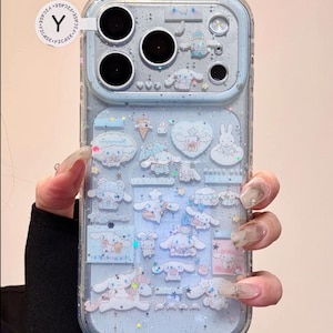 Puede incluir: Funda de teléfono transparente con fondo azul claro y purpurina. La funda presenta múltiples diseños de personajes de dibujos animados en blanco y azul claro. El área de la cámara es visible en la parte superior izquierda.