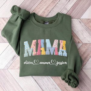 May include: Olive green sweatshirt with the word "MAMA" in colorful patchwork letters. Below the word "MAMA" are the names "oliver", "emma", and "jessica" in a script font with hearts.