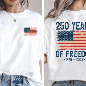A white t-shirt with a graphic design on the back, depicting an American flag with the text "250 YEARS OF FREEDOM" and "1776 - 2026" printed on it.