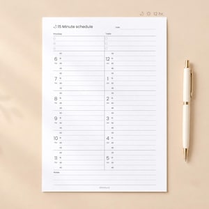 May include: A white 15 Minute schedule planner page with black text and lines, featuring columns for priorities and tasks, hourly time slots from 6 to 5, and a moon and sun icon with 12 hr. text. A cream-colored ballpoint pen lies to the right.