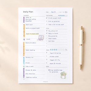 May include: A white daily planner sheet with a vertical schedule, top priorities list, to-do list, meal tracker, and notes section. The page features colourful time blocks, a small laptop icon, and a grocery bag illustration. A white pen lies beside it.