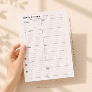 May include: A white paper planner insert with black text and lines. The header reads Weekly Overview, followed by sections for Top Priorities, Key Meetings, Deadlines, and Notes. The right side lists days from Monday to Sunday with lined spaces.