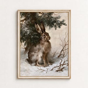 Puede incluir: Un cuadro al óleo enmarcado que representa una liebre parda sentada en un paisaje nevado bajo las ramas de un pino verde oscuro. La escena muestra ramas finas y desnudas que se extienden sobre el suelo blanco cubierto de nieve.