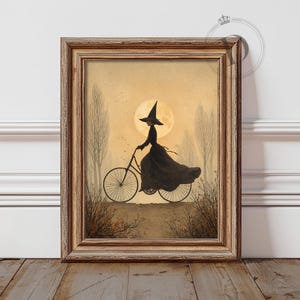 May include: Framed art print featuring a silhouetted witch riding a bicycle against a full moon backdrop. The artwork is in a vintage style, with a warm color palette of beige, brown, and black. The witch wears a pointed hat and flowing dress.