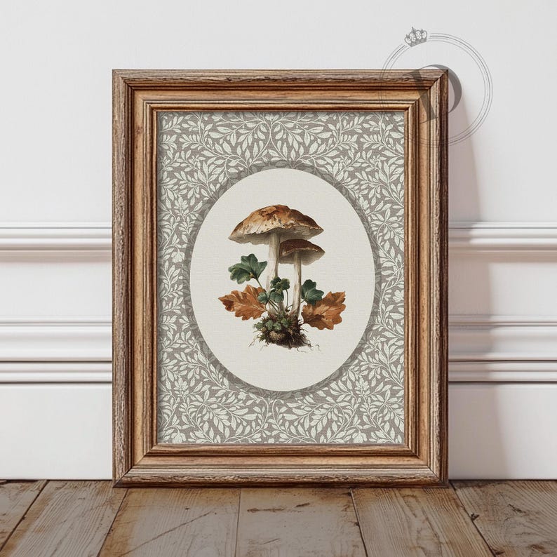 May include: A framed art print featuring a watercolor illustration of two mushrooms with brown caps and green and brown leaves. The artwork is set against a gray and white floral patterned background, within a wooden frame.