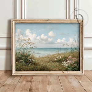 K&ouml;nnte beinhalten: Gerahmtes Landschaftsgem&auml;lde, das eine ruhige K&uuml;stenlandschaft zeigt. Das Kunstwerk zeigt einen hellblauen Himmel mit wei&szlig;en Wolken, ein ruhiges Meer und eine grasbewachsene D&uuml;ne mit Wildblumen. Der Rahmen hat eine helle, nat&uuml;rliche Holzfarbe.