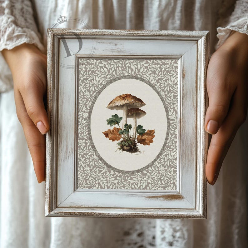 May include: A framed botanical print featuring two mushrooms with brown caps and green and brown leaves. The artwork is set against a gray and white floral patterned background, encased in a distressed white wooden frame.