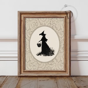 May include: Framed art print featuring a black silhouette of a witch carrying a basket, set against a cream-colored oval. The background has a beige floral pattern. The wooden frame adds a rustic touch to the artwork.