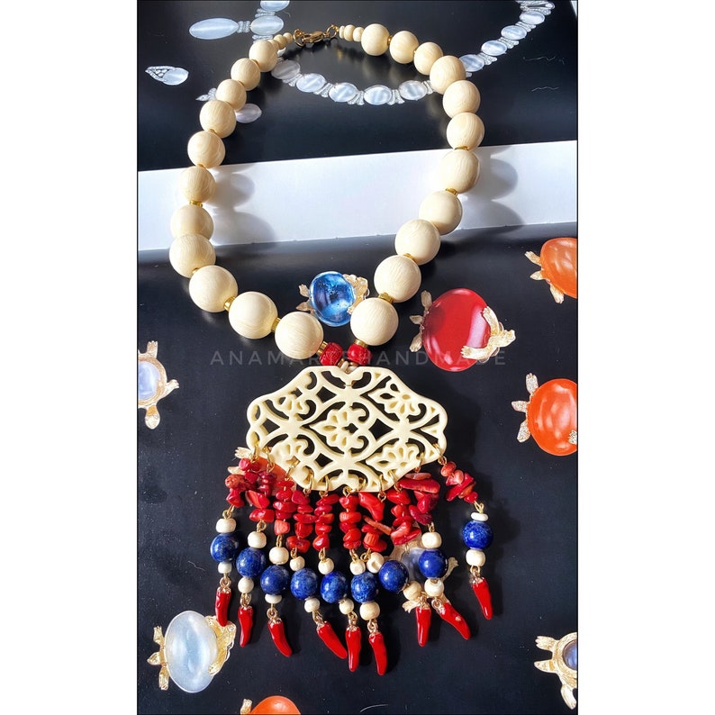 May include: A white bead necklace with a carved ivory pendant and red and blue tassel. The pendant has a floral design.